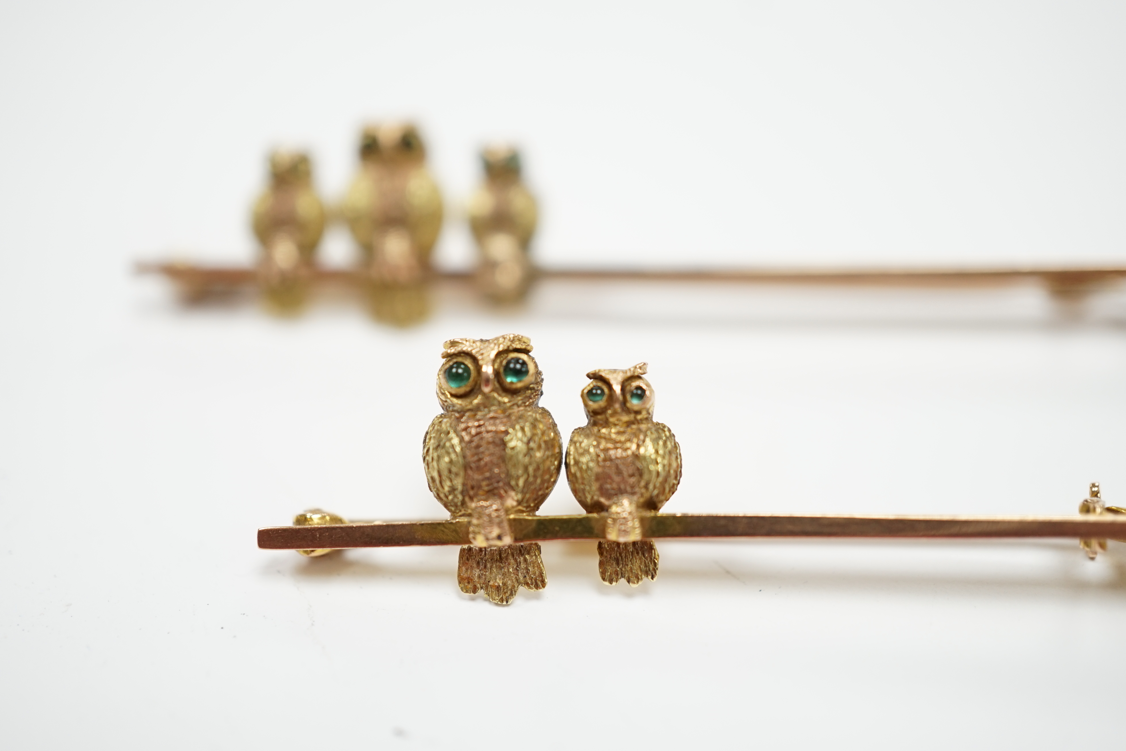 Two early 20th century 9ct owl bar brooches, with cabochon set eyes, largest 63mm, gross weight 6.9 grams.